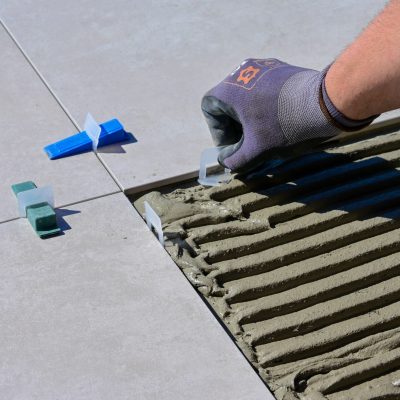 Detailed view of gloved hand aligning tiles with levelers and spacers during construction.